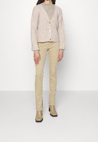 Světlounce růžový pletený kardigan s výstřihem do V, zapínáním na knoflíky vpředu a žebrovanými manžetami, doplněný krémovými strukturovanými úzkými kalhotami a béžovými botami na podpatku.