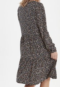 Svart blommig klänning med långa ärmar, samlad midja och lager på lager kjol. Har små rosa och blå blommor på en mörk bakgrund.