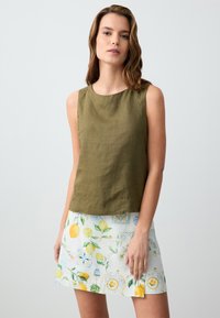 Top senza maniche in lino verde oliva abbinato a una gonna bianca con un motivo di limoni e fiori nei toni del giallo e del blu.