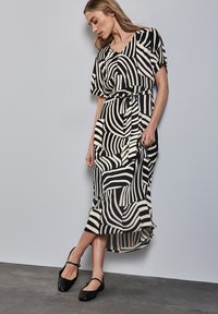 Zwart en crème gestreepte maxi-jurk met korte mouwen, een tailleband en een vloeiende silhout. Gemaakt met zwarte platte schoenen.