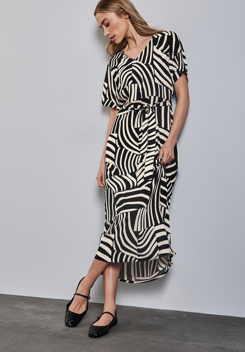 Zwart en crème gestreepte maxi-jurk met korte mouwen, een tailleband en een vloeiende silhout. Gemaakt met zwarte platte schoenen.