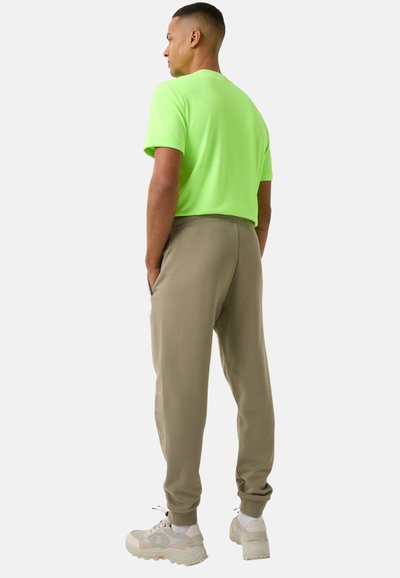 Neon groene t-shirt met korte mouwen gecombineerd met beige joggingbroek, voorzien van een elastische taille en geribbelde manchetten, gedragen met beige sneakers.