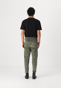 Un t-shirt noir à manches courtes se marie avec un pantalon en velours côtelé vert olive muni d'une taille élastique. Des bottines noires viennent compléter la tenue.