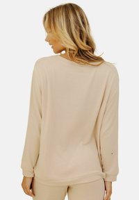 Haut beige à manches longues avec un col rond et une coupe ample. Tissu doux avec des poignets légèrement retroussés et un design épuré et simple.