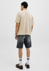 Beige mintás, galléros, rövid ujjú ing, sötét farmer sorttal párosítva, fehér zokni fekete csíkokkal, és barna cipőkkel.