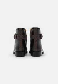 Bottines en cuir noir avec un motif texturé marron, des accents en métal doré et un talon plat robuste, dotées d'une fermeture éclair sur le côté.