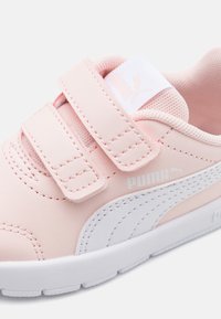 Baskets Puma rose clair avec deux bandes auto-agrippantes, logo Puma blanc sur le côté et semelle blanche, conçues pour un enfilage facile.