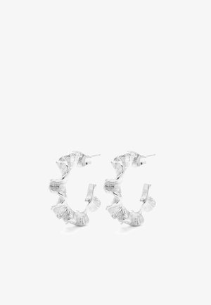 Paire de boucles d'oreilles créoles argentées texturées avec bords ondulés et irréguliers, fermoirs à tiges, sur fond blanc.