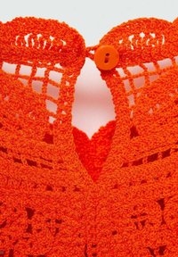 Nahaufnahme von leuchtend orangefarbigem gehäkeltem Stoff mit Blumenmustern und einem passenden Knopfverschluss am Halsausschnitt eines Kleidungsstücks.
