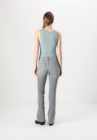 Top a righe di colore blu chiaro abbinato a pantaloni flared grigi chiari con tasche posteriori decorative e una texture liscia. Stivali neri con tacco.