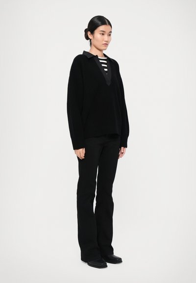 Black oversized knit sweater with a V-neck, paired with a black and white striped top, black flared pants, and flat black shoes.