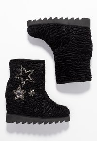 Botines negros de terciopelo texturizado con suelas gruesas y estriadas, adornados con tres parches decorativos de estrellas con lentejuelas en el lado exterior.