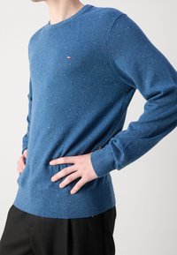 Niebieski sweter z okrągłym dekoltem wykonany z dzianiny o fakturze z kolorowymi kropkami. Posiada prążkowane mankiety i dół oraz małe logo.