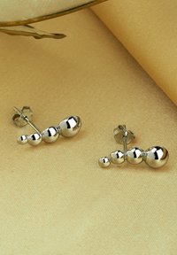 Silversmycken med stift som har en serie av graderade sfäriska former, med polerad yta, belägna mot en beige tygbakgrund.