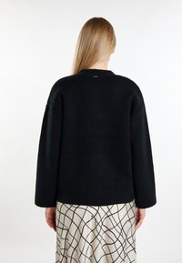 Schwarzer, gestrickter Pullover mit lockerer Passform, weiten Ärmeln und einfachem Rundhalsausschnitt. Leicht strukturierter Stoff, niedriger Rückenschnitt.