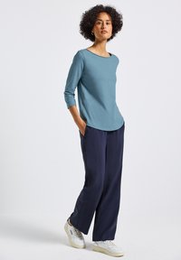 Top blu chiaro a maniche lunghe con collo arrotondato, abbinato a pantaloni larghi blu navy e sneakers bianche. Tessuto morbido, vestibilità casual.