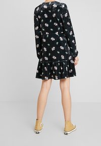 Svart sammetklänning med blommönster, långa ärmar och volang i nederkant. Bärs med beige ankelstövlar med vita sulor och snören.