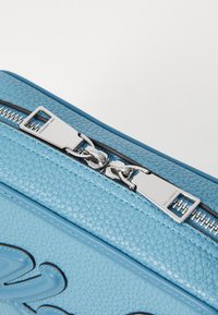 Geantă din piele bleu deschis cu un finisaj texturat, dotată cu un fermoar și accesorii din argint, având detalii debossate pe suprafață.