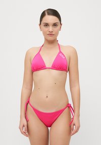 Rožinė trikampė bikini maudymosi kostiumėlis su plonomis petnešėlėmis ir surišamais šonais. Pagamintas iš minkštos, lygios medžiagos. Papuoštas subtiliu logotipu. 