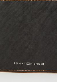 Black textured wallet featuring orange stitching and embossed logo "TOMMY HILFIGER" in white. Smooth finish with sleek rectangular shape.
