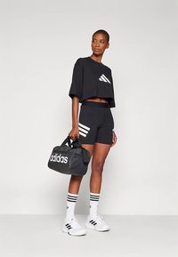 Μαύρο κοντό τοπ με λευκό λογότυπο, μαύρο σορτς που ταιριάζει, λευκά αθλητικά παπούτσια και μαύρη τσάντα duffel με λευκή σήμανση. Ριγέ κάλτσες.