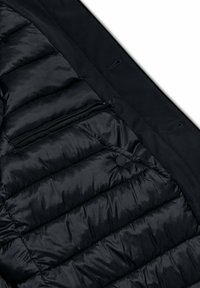 Zwarte pufferjacksectie met gestikt ontwerp. Bevat een ritszak en drukknoop. Zachte textuur met matte afwerking.