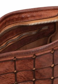 L'interno della borsa in pelle marrone presenta una texture intrecciata, due tasche con zip e un rivestimento in tessuto liscio. I denti della zip sono di colore argento.