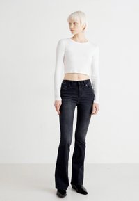 Black flared jeans and a cropped white long-sleeve top. The outfit features a fitted design and smooth texture. Footwear is pointed black heels.