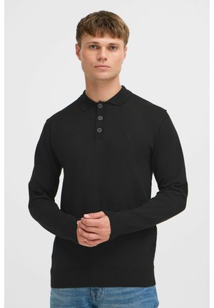 Zwarte langlopende poloshirt met een drieknopsplacket en geribbelde manchetten, gedragen door een persoon tegen een neutrale achtergrond.