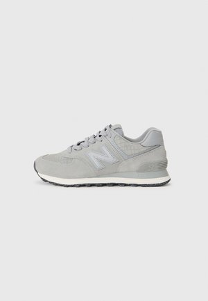 Grå New Balance sportssko i ruskind og mesh med snørelukning og mønstret hældetalje, vist i profil set på lyse baggrund.