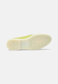 Sål i hvid gummi med cirkulære grebmønstre. Overdel i lys gul med en glat tekstur og prægning af mærket.