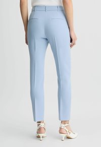 Pantaloni azzurri su misura con una texture liscia, dotati di tasche posteriori e un design aderente. Indossati con sandali con tacco bianchi.