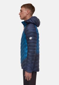 Blauer Daunenjacke mit Kapuze, ausgestattet mit einer Mischung aus horizontalen und Zickzack-Steppdesigns. Akzentuiert mit orangefarbenen Reißverschlüssen und einem Logo am Ärmel.