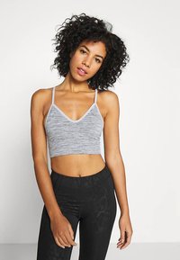 Brassière de sport grise coupée avec un motif chiné subtil, encolure en V et fines bretelles, associée à des leggings noirs texturés taille haute.
