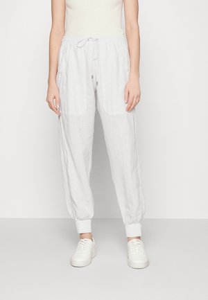 Persona vistiendo pantalones jogger blancos con cordón y puños elásticos, combinados con zapatillas blancas y una camiseta sin mangas de tejido acanalado.