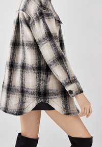 Černobílá kostkovaná flanelová košile, texturovaná látka, dlouhé rukávy, manžety na knoflíky, zakulacený spodní lem, volný střih, pohled zezadu.