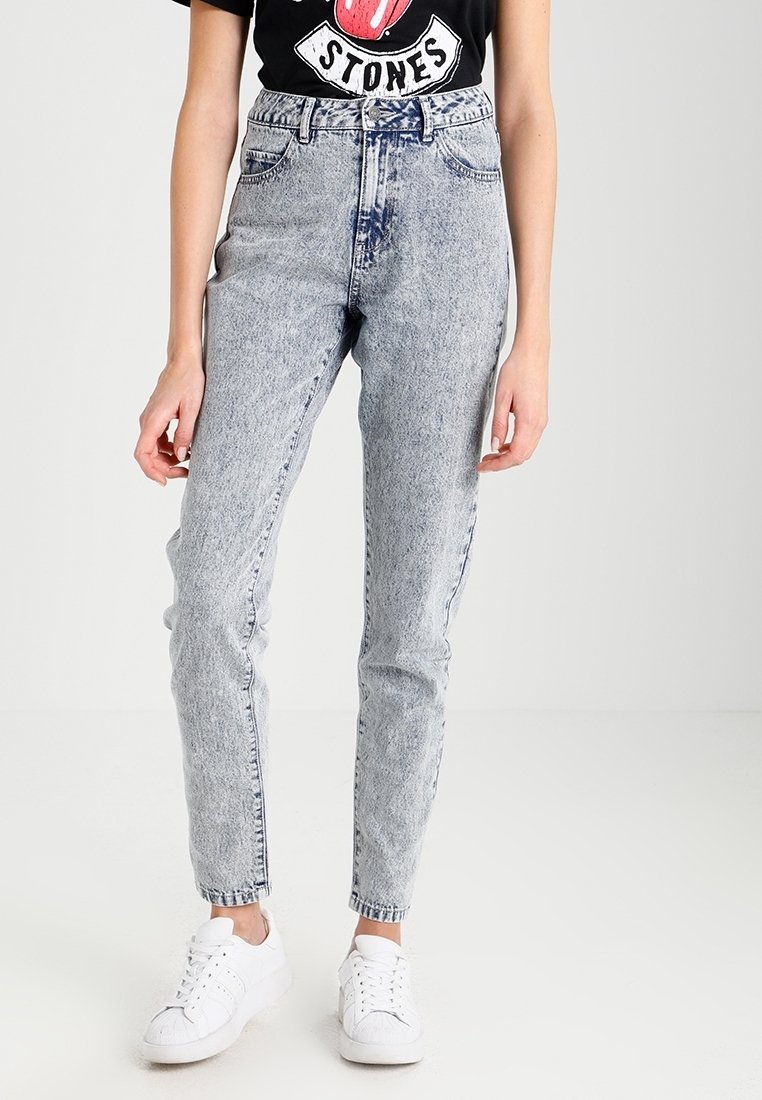 Jeans de talle alto, de color azul claro, con un efecto de lavado ácido, ajuste tapered y bolsillos frontales, combinados con una camiseta gráfica negra y zapatillas blancas.