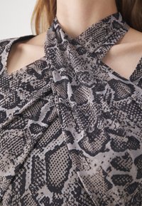 Femme portant un haut à col halter imprimé serpent noir et gris avec des bretelles croisées et des épaules dénudées.