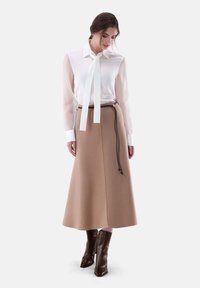 Blusa bianca con maniche trasparenti e un nodo al collo, abbinata a una gonna beige a trapezio e stivali alla caviglia marroni. Design minimalista con linee pulite.