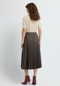 Hame lungi plisată din material maro închis, asociată cu un top cu mânecă scurtă de culoare crem și botine burgund cu fermoar și detalii aurii.