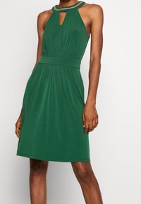 Robes halter vert avec un décolleté à trou de serrure, taille élastique et texture de tissu lisse. Présente un ornement complexe le long du cou et une silhouette fluide.