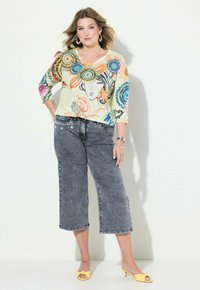 Maglia a maniche lunghe multicolore e a fantasia con scollo a V, abbinata a jeans cropped grigi con dettagli decorativi. Sandali con tacco gialli.