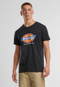 Juodas medvilninis marškinėliai su spalvingu "Dickies" logotipu, kuris yra centre ant krūtinės. Trumpomis rankovėmis ir apvaliu kaklu. Kasdienis kirpimas.