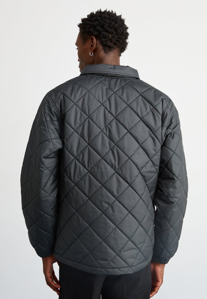 Chaqueta negra acolchada con un ajuste relajado, que presenta un cuello clásico y puños elásticos, fabricada con un material suave y ligero.