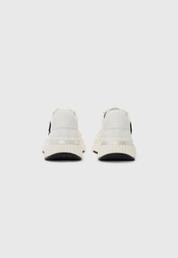 Sneakers bianchi con suola in gomma texturizzata, materiale superiore liscio e accento nero. Presentano un dettaglio riflettente sul tallone.