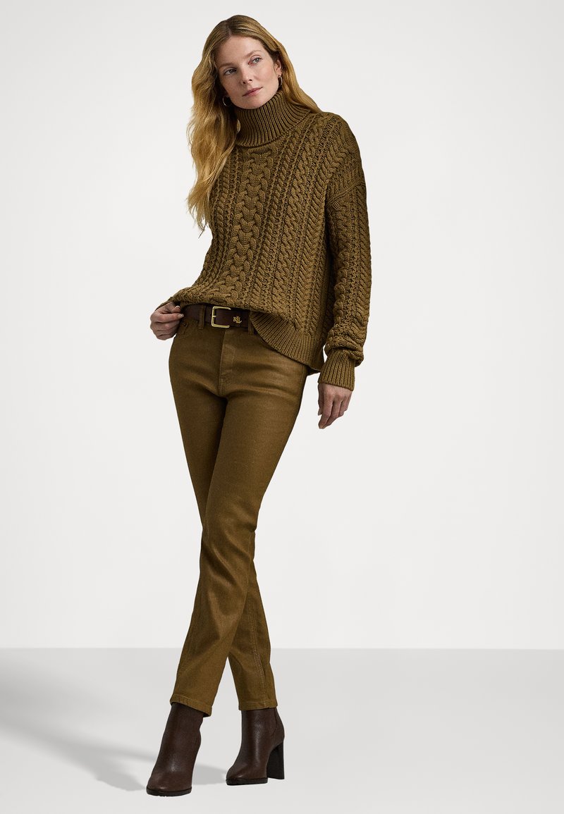 Brauner, grob gestrickter Rollkragenpullover mit gerippten Bündchen, kombiniert mit braunen, taillierten Hosen und dunklen, Absatzstiefeletten. Einfaches Metallbuckle am Gürtel.