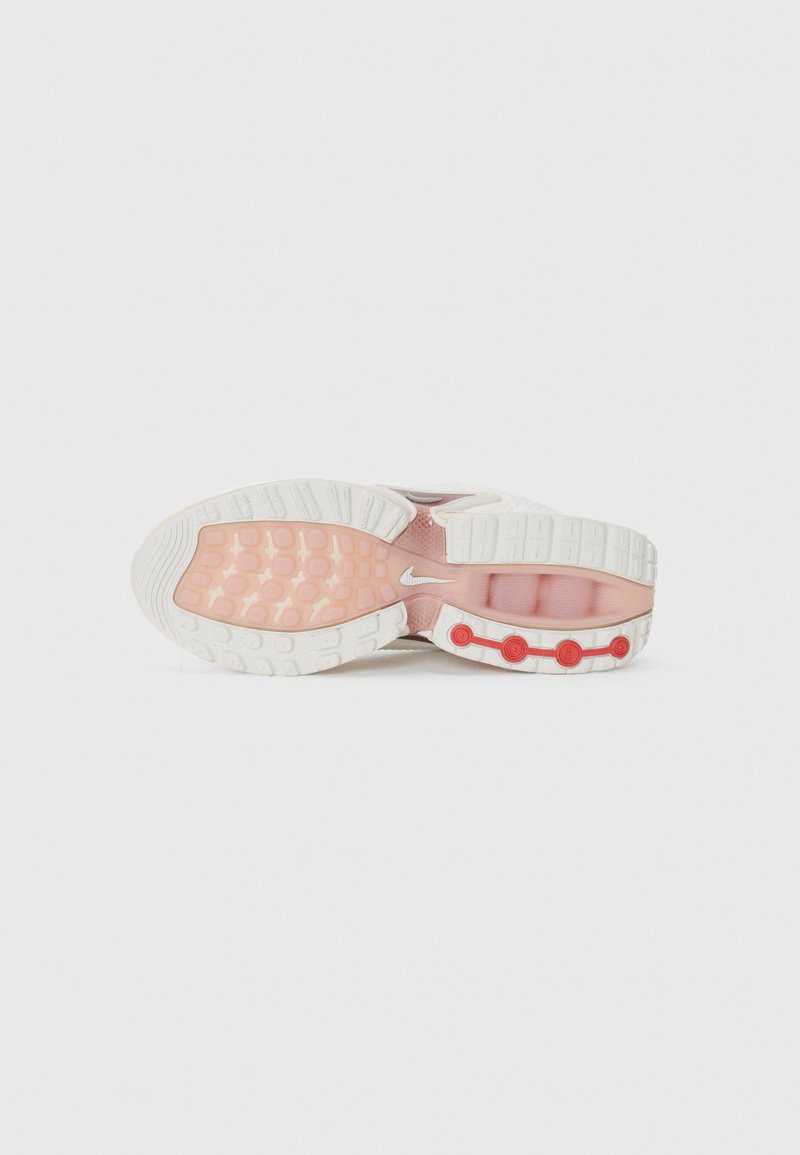 Sneaker Nike avec une semelle blanche et rose, présentant un motif en caoutchouc texturé et des accents rouges le long du côté.