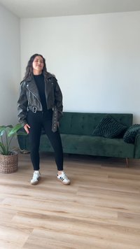 Musta nahkatakki, jossa on leveä kaulus, hopeiset yksityiskohdat ja vyö; yhdistetty mustiin legginsseihin ja valkoisiin tennareihin, joissa on mustia yksityiskohtia.