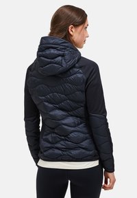 Svart och marinblå jacka med en puffy kviltad design på baksidan, utrustad med huva och åtsittande ärmar. Slen tygtextur och modern passform.