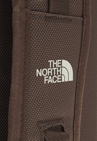 Gros plan sur un tissu marron texturé avec le logo blanc The North Face imprimé sur une sangle de sac.